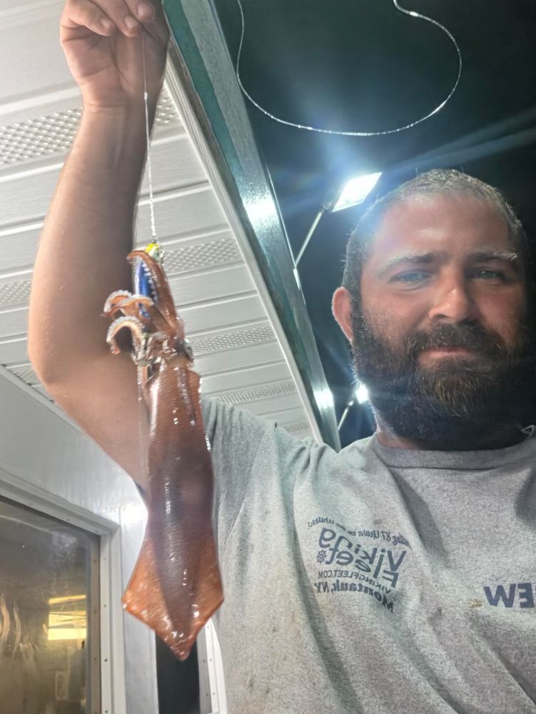 Man holding a squid under bright lights on a boat.