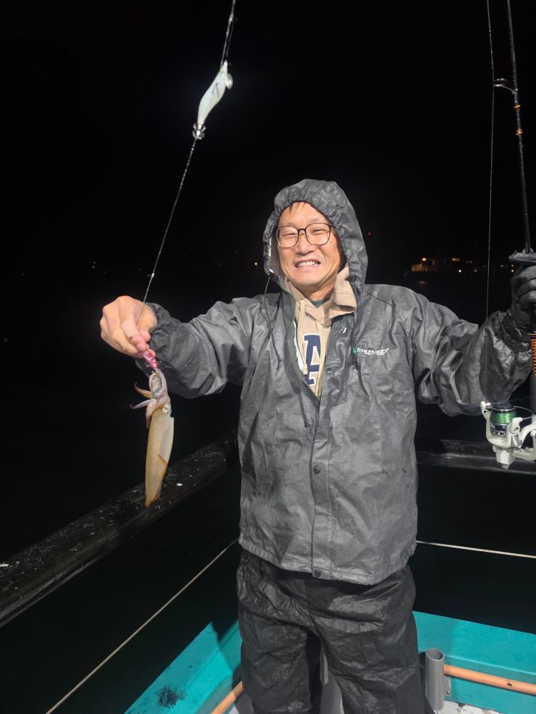 Person in raincoat holding a fishing rod and a squid on a boat at night.