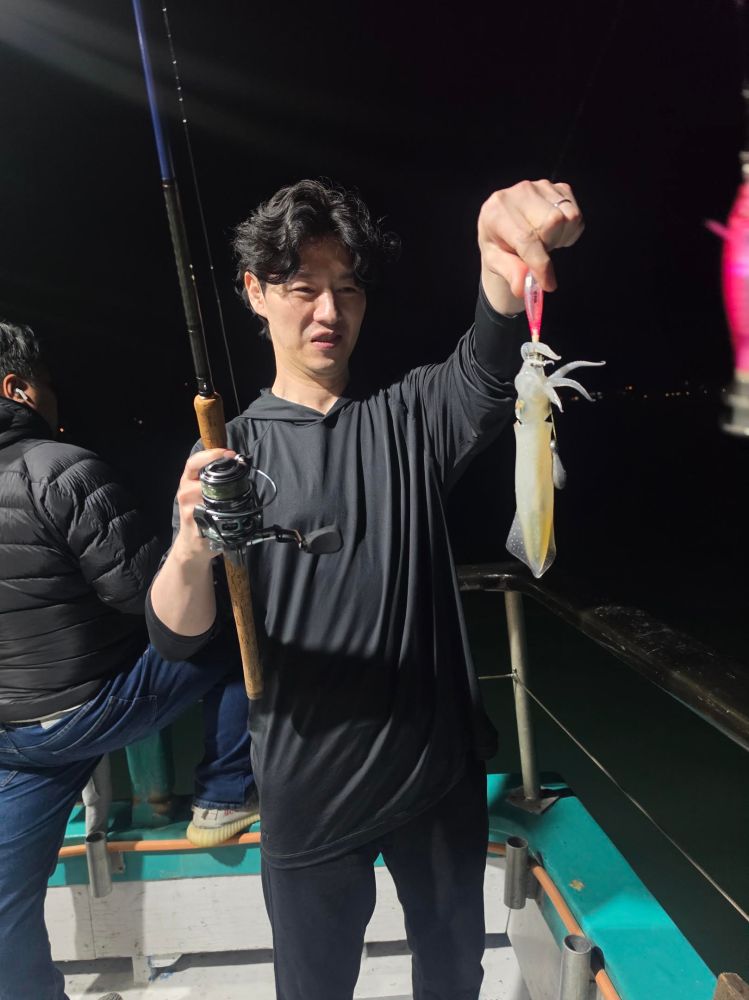 Person holding a fishing rod and a caught squid on a boat at night.