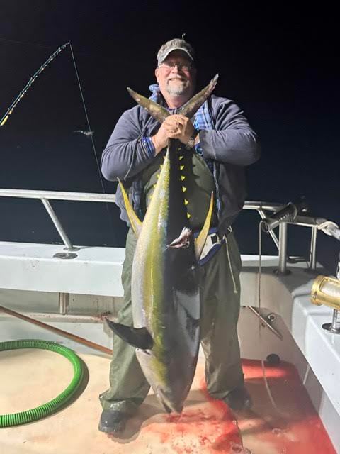 Man holding a large fish on a boat at night.
