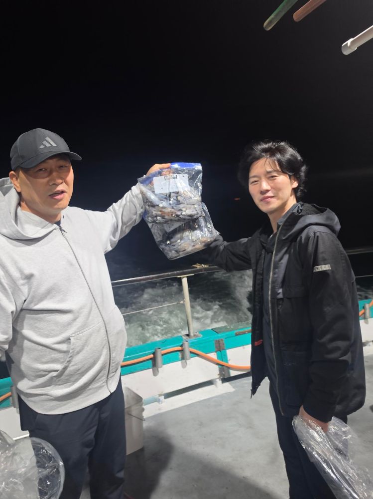 Two people on a boat at night holding a bag of fish.