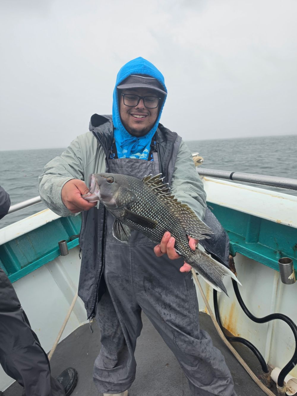 Person on boat holding a large fish in rainy weather.