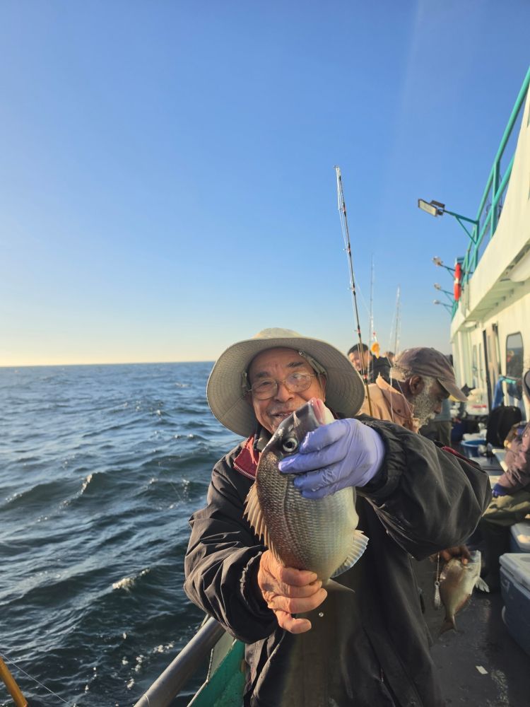 Person wearing hat and gloves holding a fish on a boat at sea.