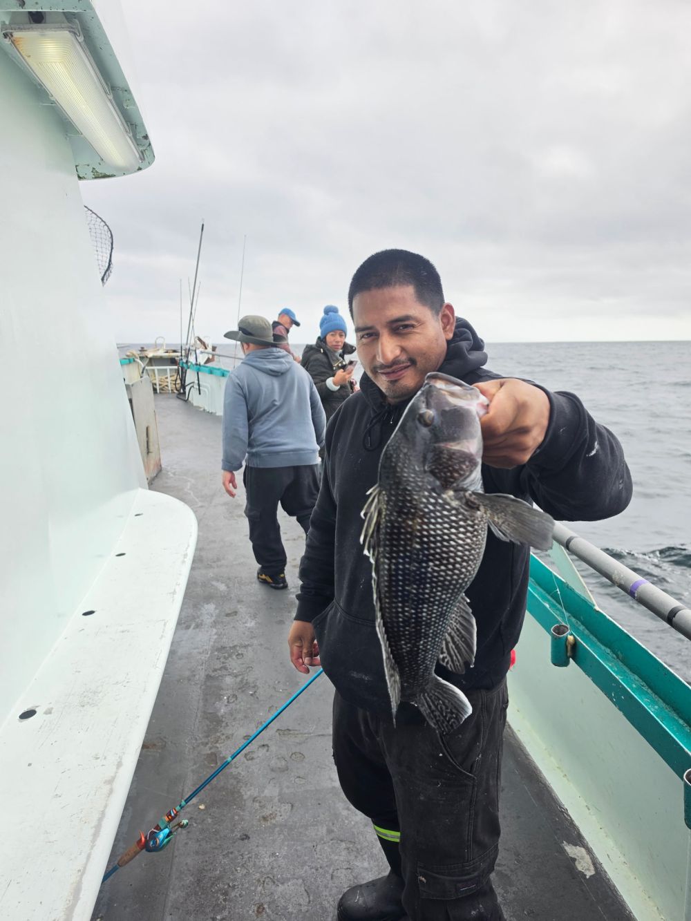Man on boat holding a freshly caught fish with others in the background.