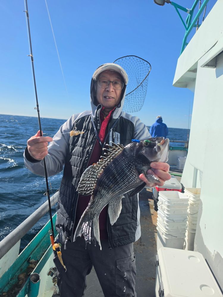 Person holding a fish on a boat, wearing a jacket and cap.