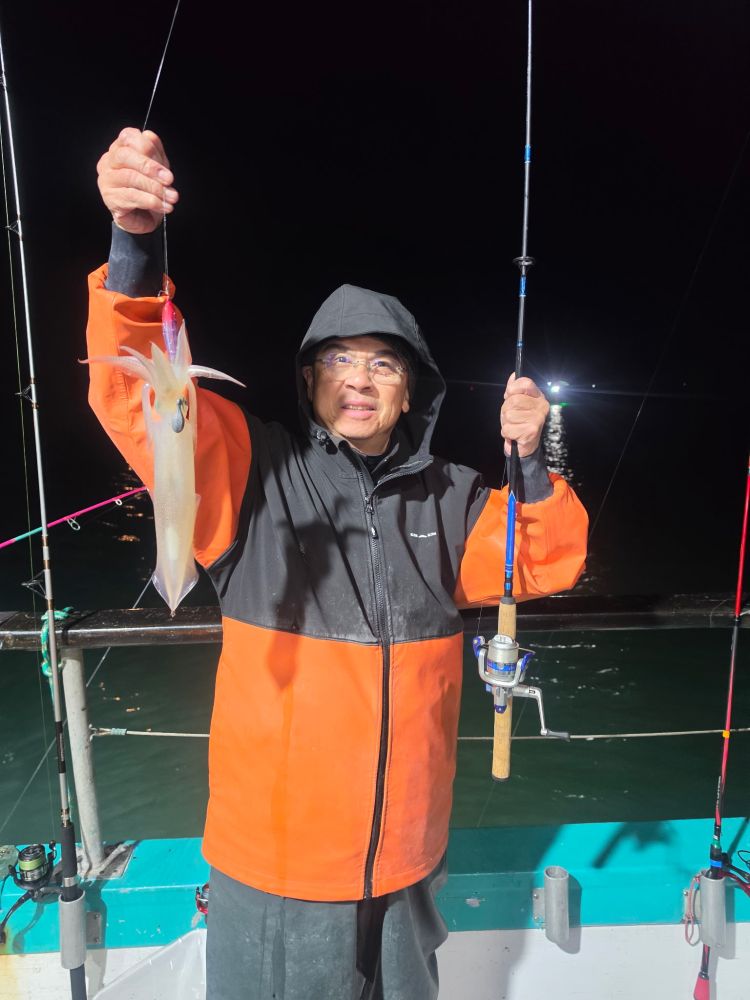 Person in raincoat holding a squid on a boat at night.