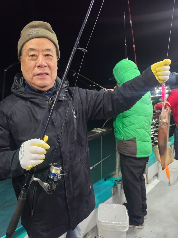 Man on a boat at night holding fishing rod with a caught squid.
