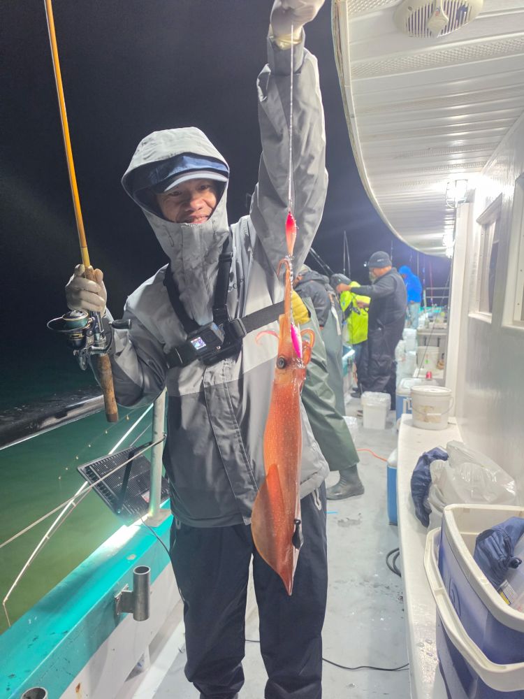 Person on a boat holding a fishing rod with a squid catch at night.