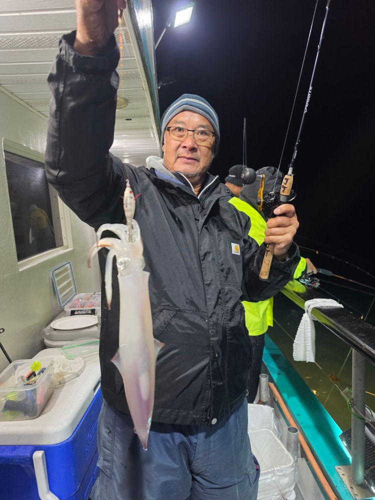 Person holding a squid while fishing at night on a boat.