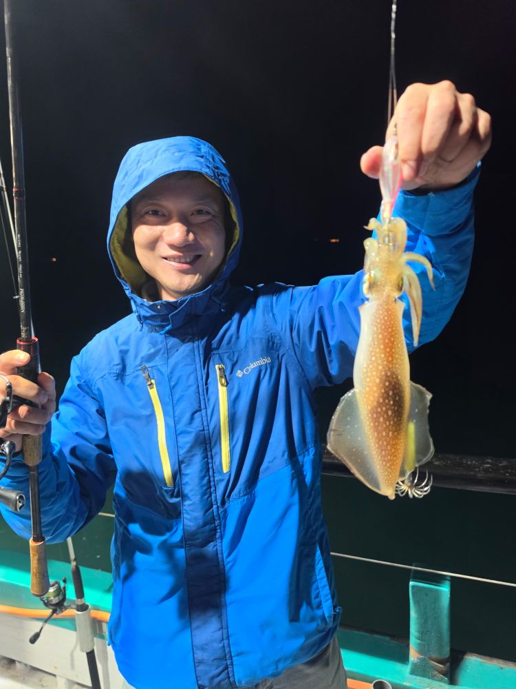 Person in blue jacket holding a caught squid on a fishing rod at night.