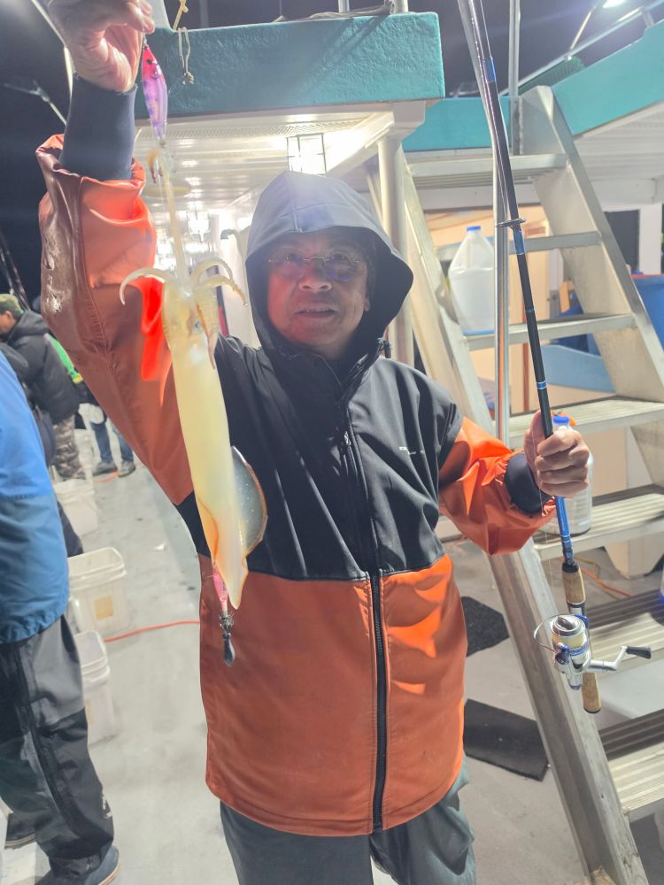 Person on a boat holding a fishing rod and a caught squid at night.