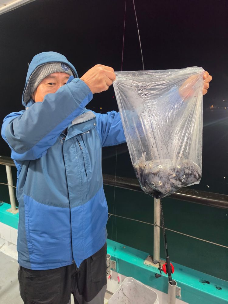 Person holds a clear bag full of fish on a boat at night.