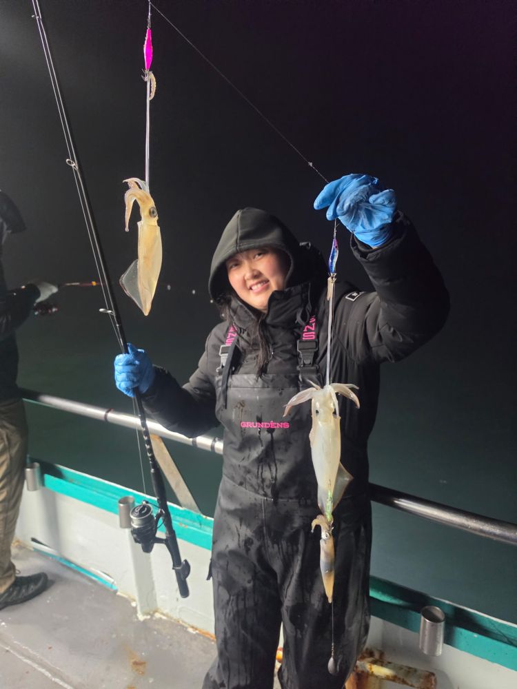 Person on a boat holding a fishing rod with caught squids at night.