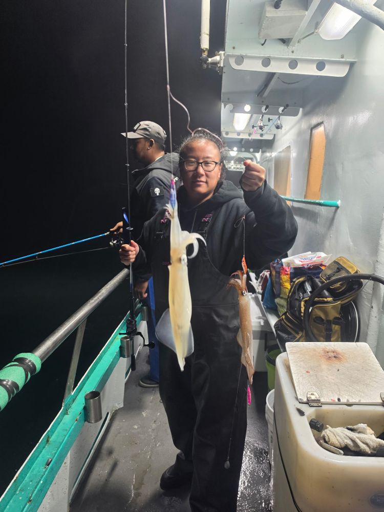 Person on a boat holding a fishing rod with a squid at night.