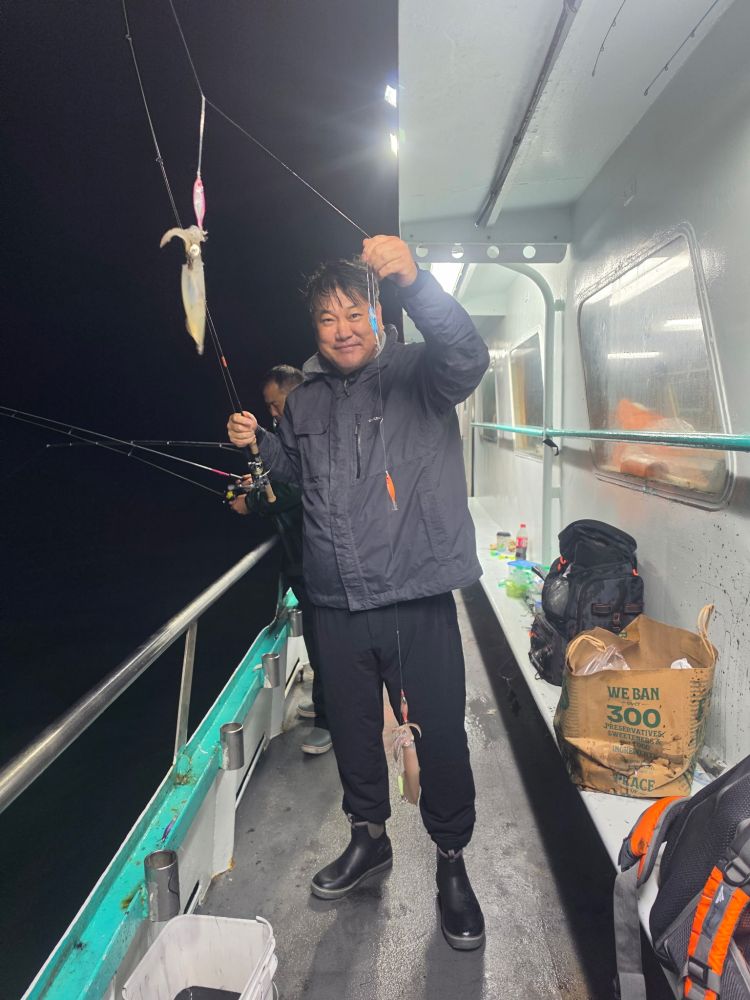 Person on a boat at night holding a fishing rod with a caught fish.