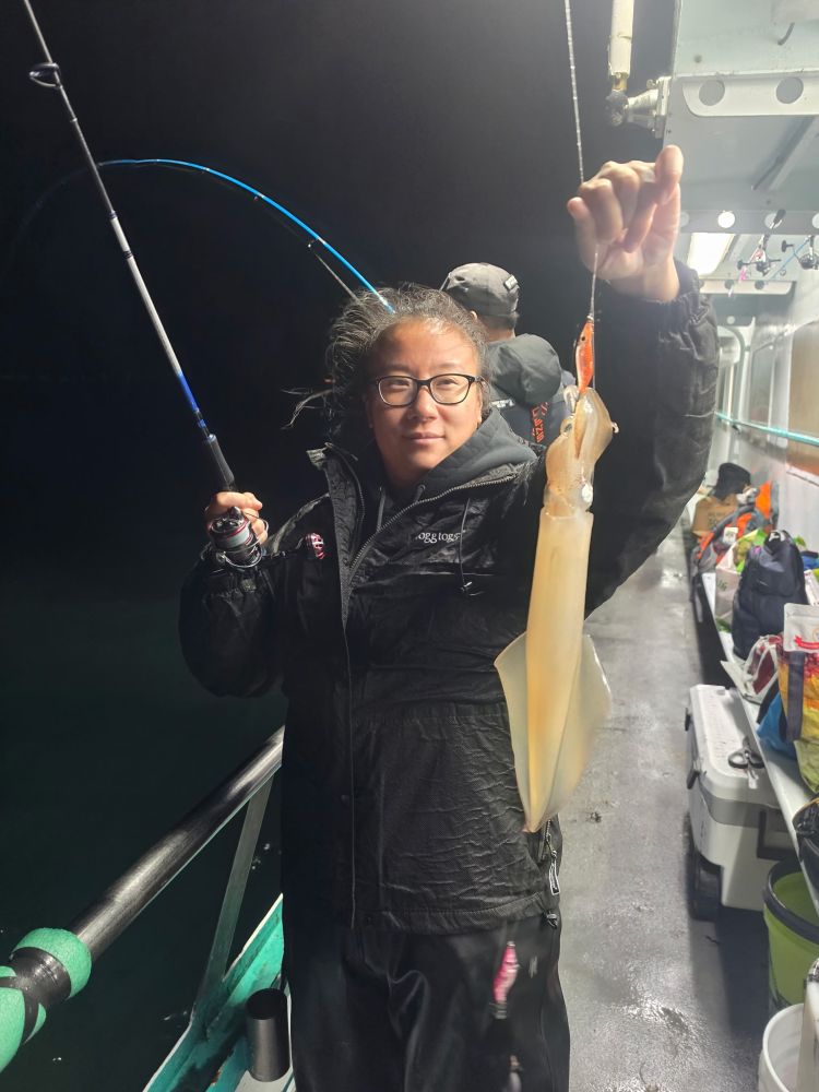 Person holding a squid on a fishing line aboard a boat at night.