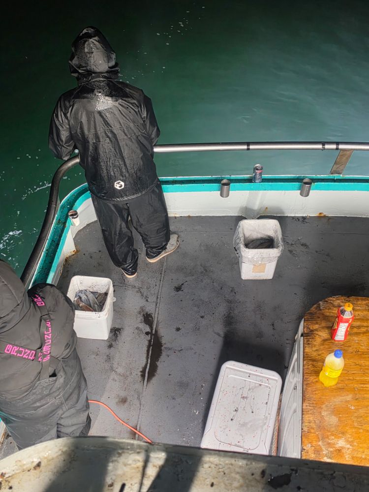 Two people in rain gear fishing on a boat at night.