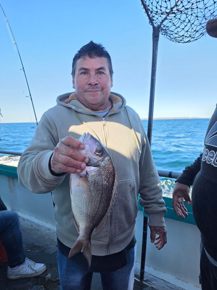 Person holding a fish on a boat, with ocean in background.