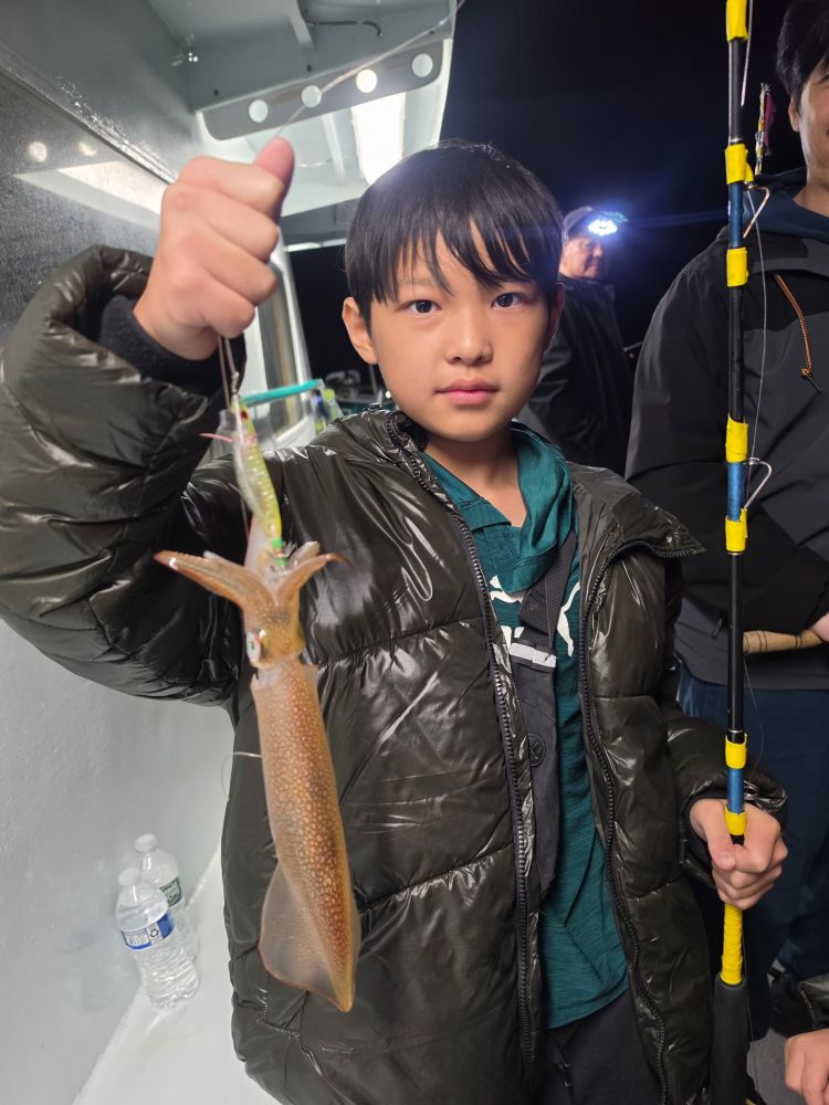 Child holding a squid on a fishing line inside a boat.