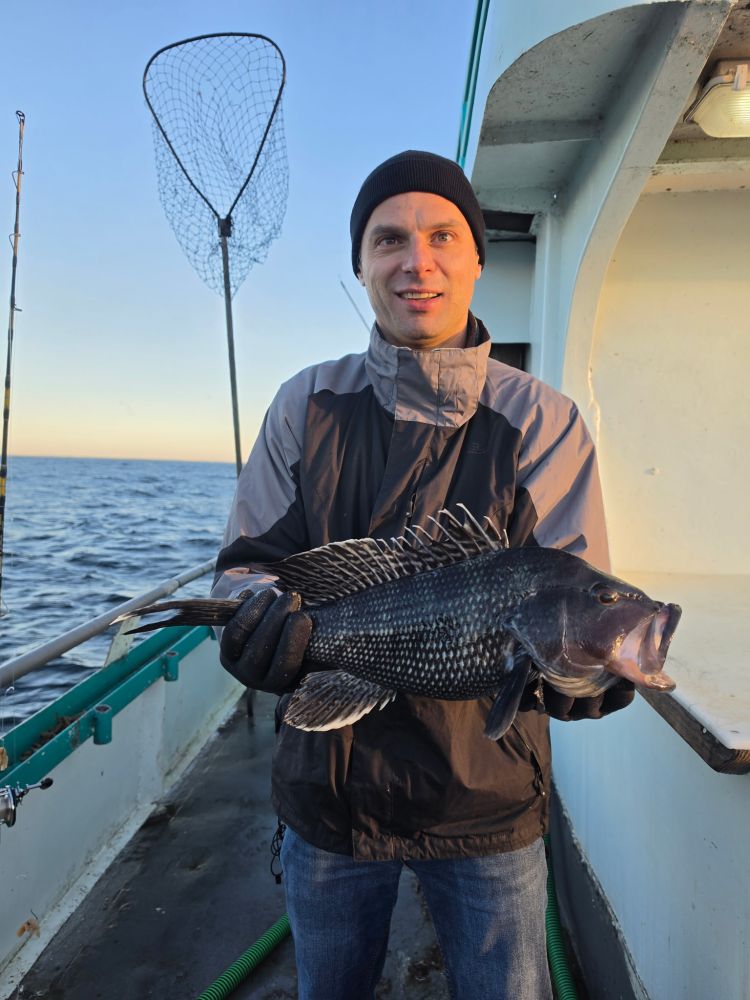 Person holding a large fish on a boat with a fishing net in the background.