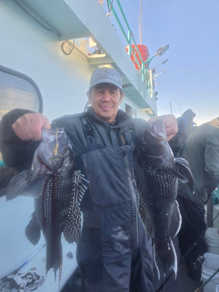Person on boat holding two large fish, wearing a cap and raincoat.