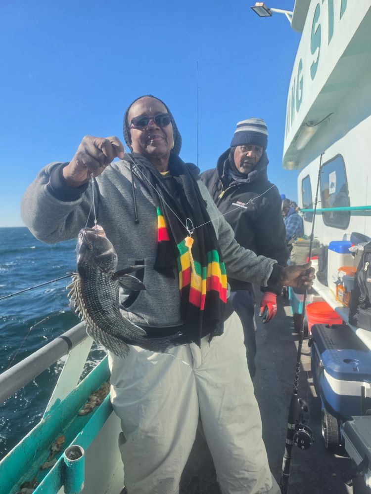 Two people on a boat with a fish, one holding a fishing rod.