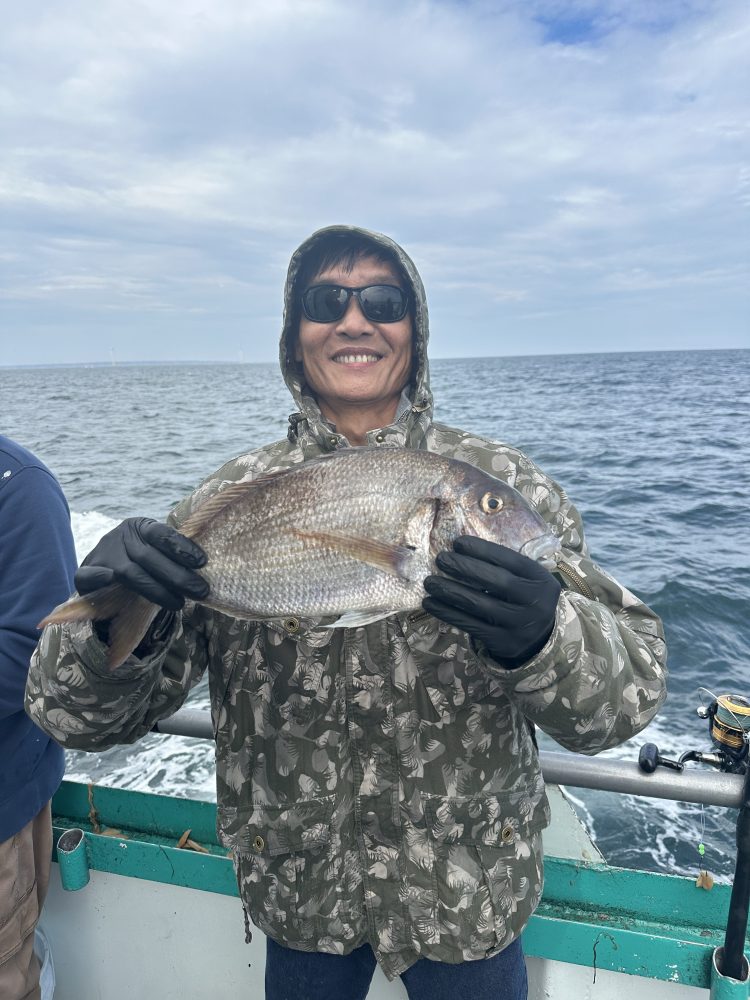 Person in camo jacket holding a large fish on a boat with ocean background.