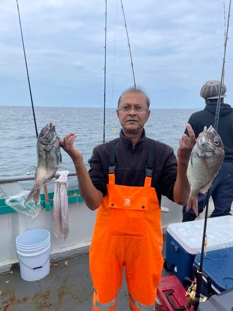 Person on boat holding two fish, wearing orange overalls.