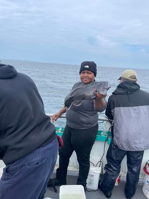 Person holding a fish on a boat with others fishing nearby.