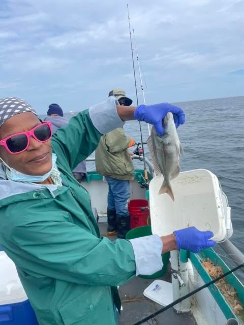 Person on a boat holding a fish, wearing gloves and sunglasses.