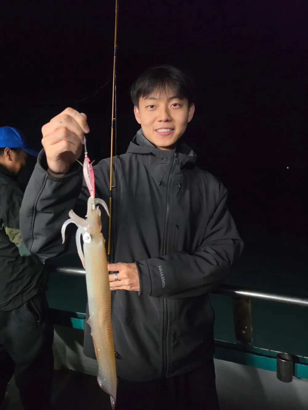 Person holding fishing rod with squid at night on a boat.