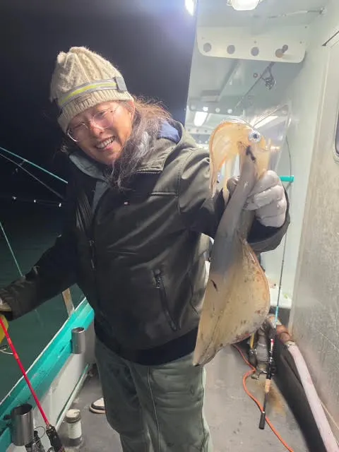 Person on a boat holding a large squid at night.