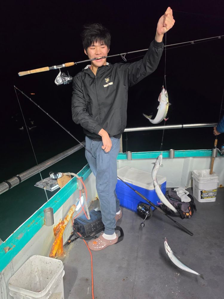 Person on a boat holding a fishing rod with a caught fish at night.