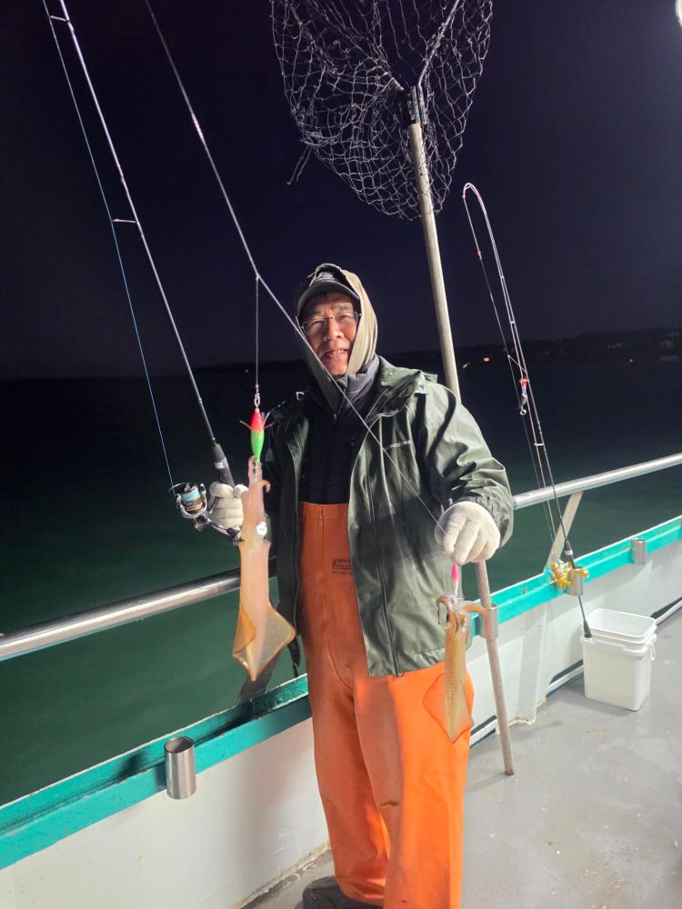 Person in orange overalls holding fishing rods with squid on a boat at night.