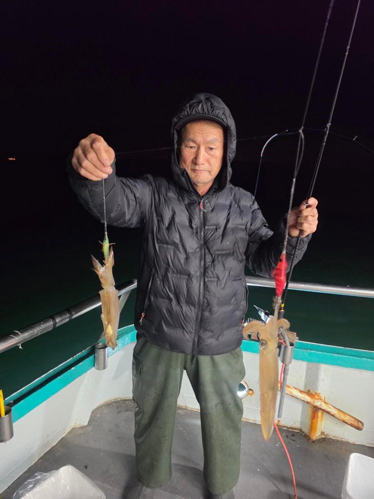 Person holding two squid while fishing on a boat at night.