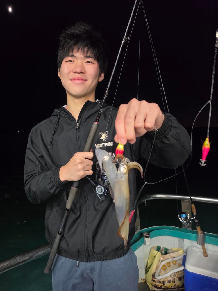Person holding a fishing rod and a caught squid on a boat at night.