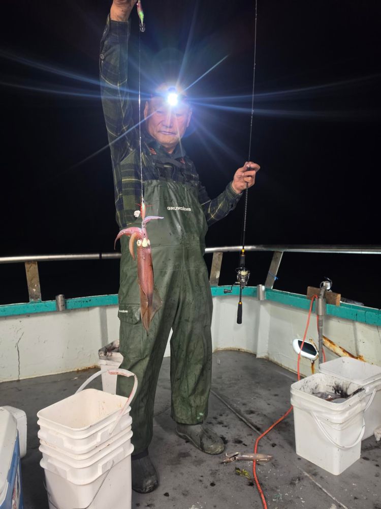 Angler on boat holding squid at night, wearing headlamp.