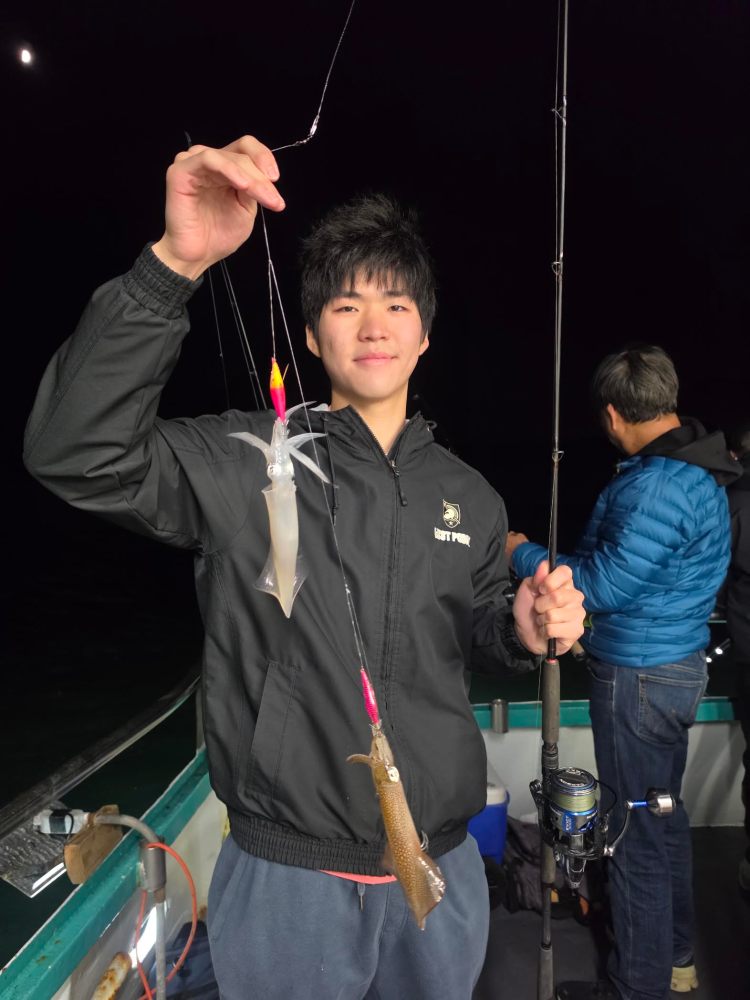 Person holding fishing rod with caught squids on a boat at night.