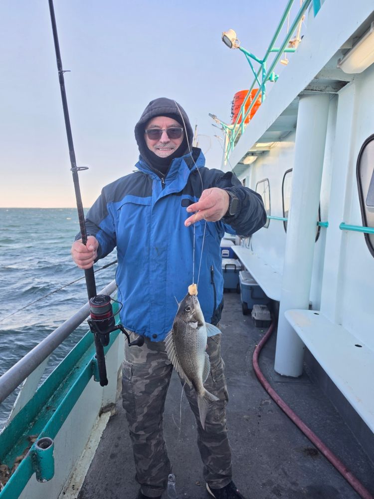 Person in blue jacket holding fish on boat deck.