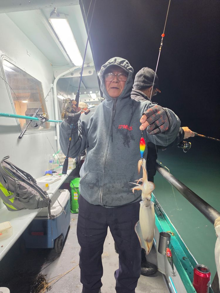 Person on a boat holding a caught squid with fishing rod at night.