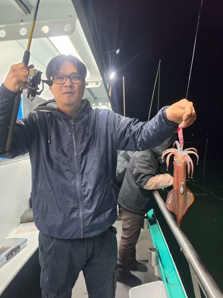 Person on a boat at night holding a fishing rod with a squid.