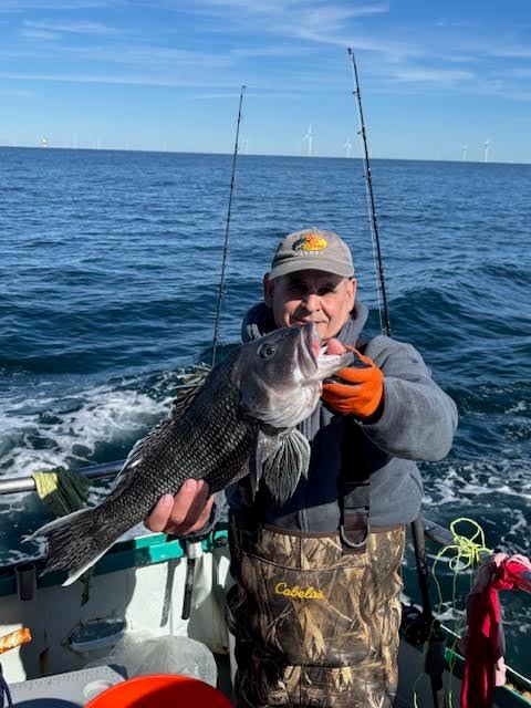 Person on boat holding a large fish, ocean and wind turbines in background.