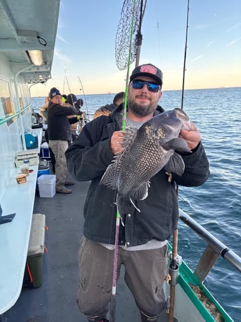 Man on boat holding a large fish with several people fishing nearby.