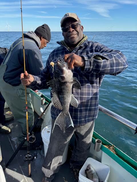 Man holding a fish on a boat with another person fishing.
