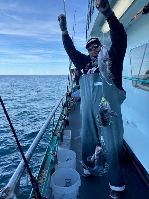 Person on boat holding caught fish with blue sea and sky in background.
