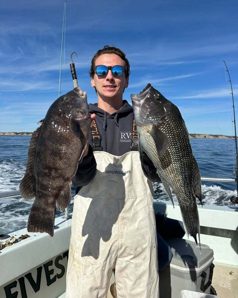 Person on a boat holding two large fish with the ocean in the background.
