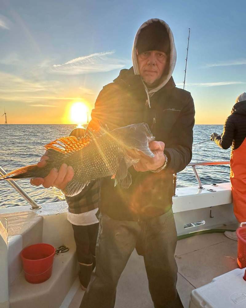 Person holding a fish on a boat at sunset with another person nearby.