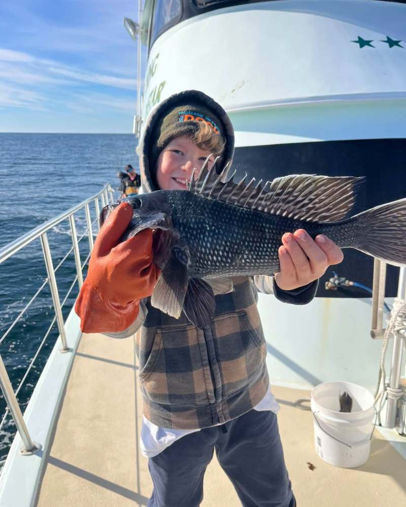 Child holding a fish on a boat with ocean in background.
