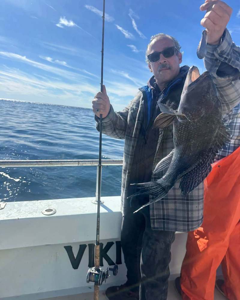 Man on boat holding a large fish with a sunny ocean backdrop.