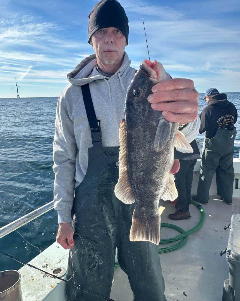 Man holding a fish on a boat with others fishing nearby.